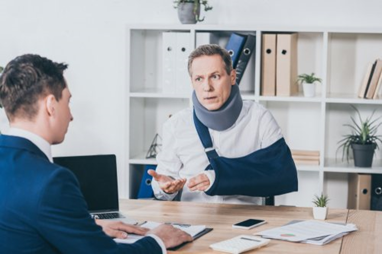 man with orthopedic collar and arm in cast, talking to man in suit in office