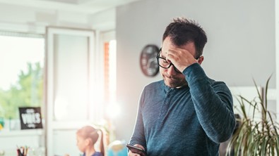 man looking at phone with a hand on his head worried
