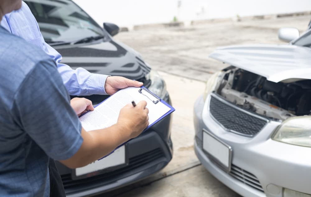 Insurance professional documents details on a clipboard as another assesses damage to a black car post-accident.