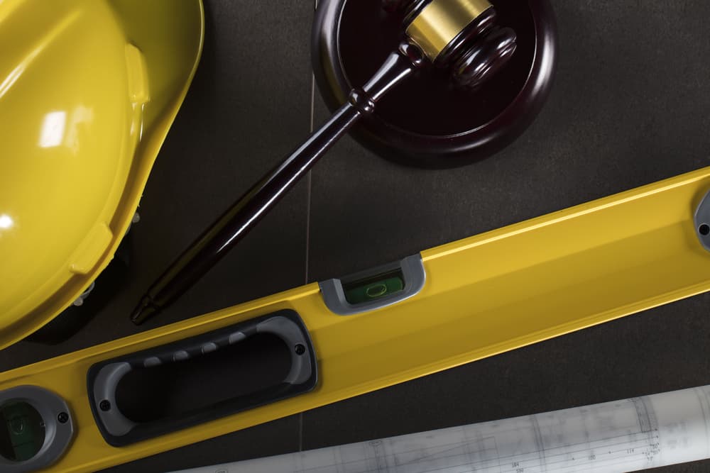 A yellow hard hat, gavel, spirit level, and architectural plans on a dark surface.