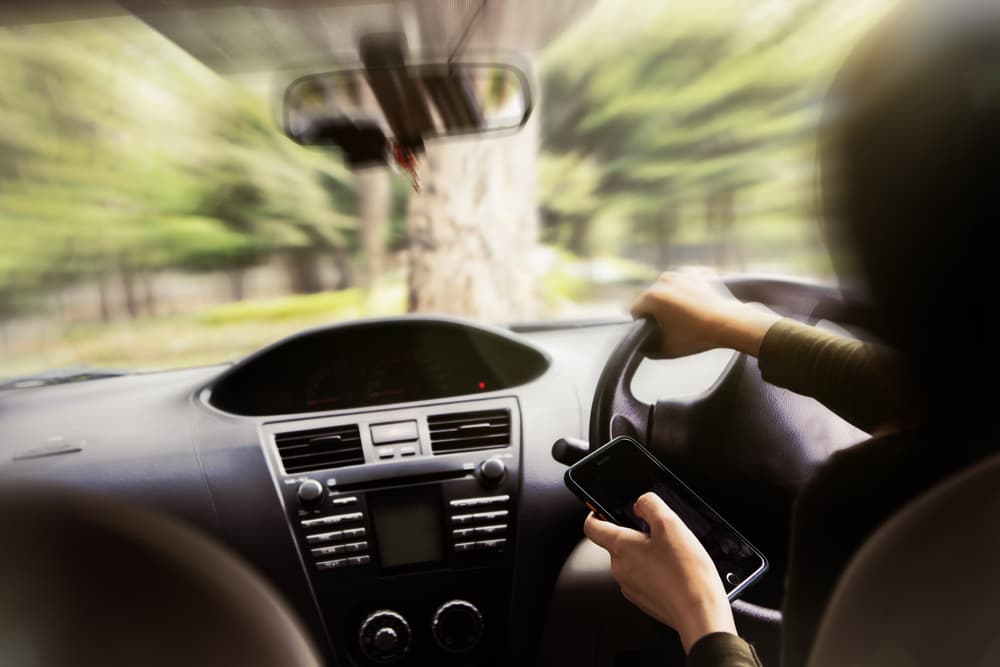 Conductor distraído con su smartphone mientras conduce, lo que supone un riesgo importante de accidente de tráfico.