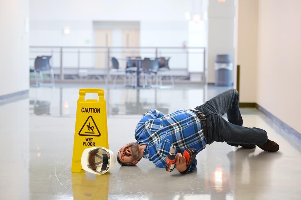 A worker slips on a wet floor and cries out in pain.