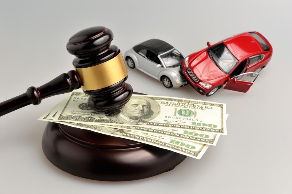 A judge gavel with money and toy cars on gray background.