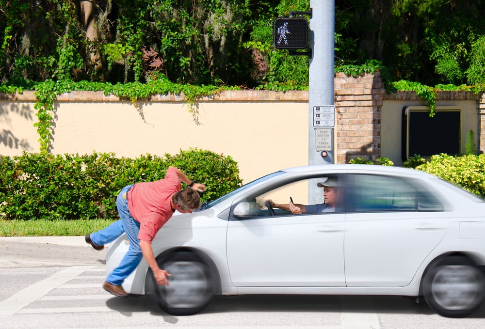 A pedestrian to be hit by a moving car at a crosswalk, driver looks unaware.