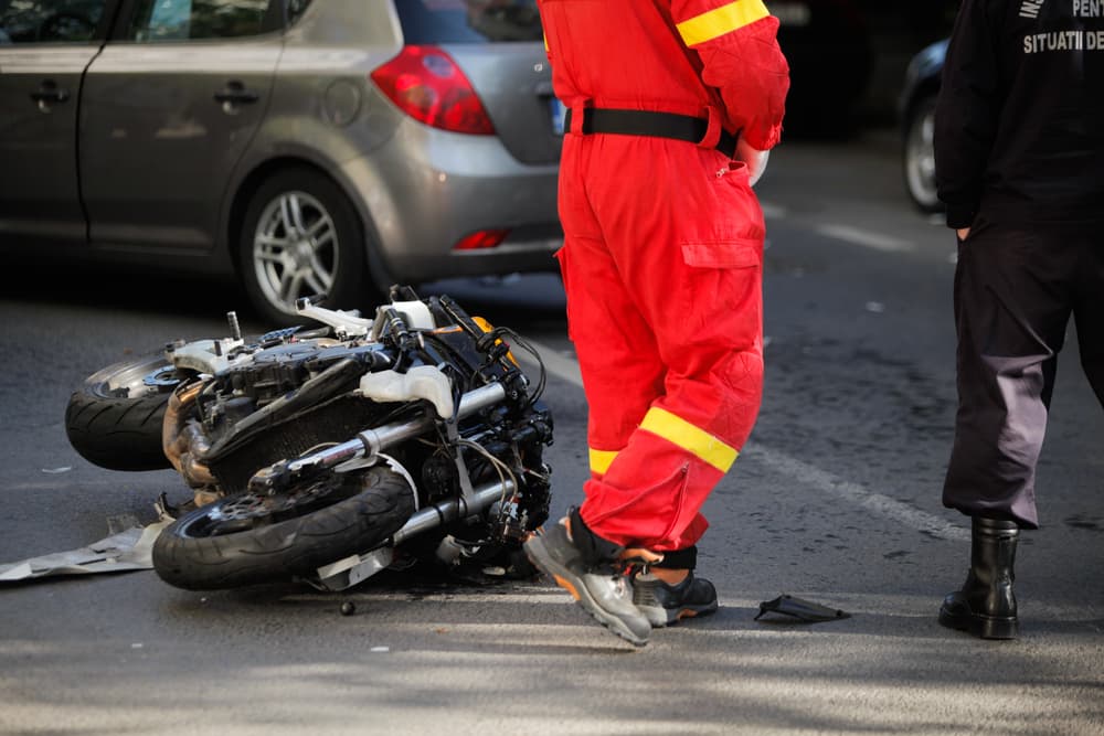 Emergency responder at a motorcycle crash scene with a toppled bike on the road.