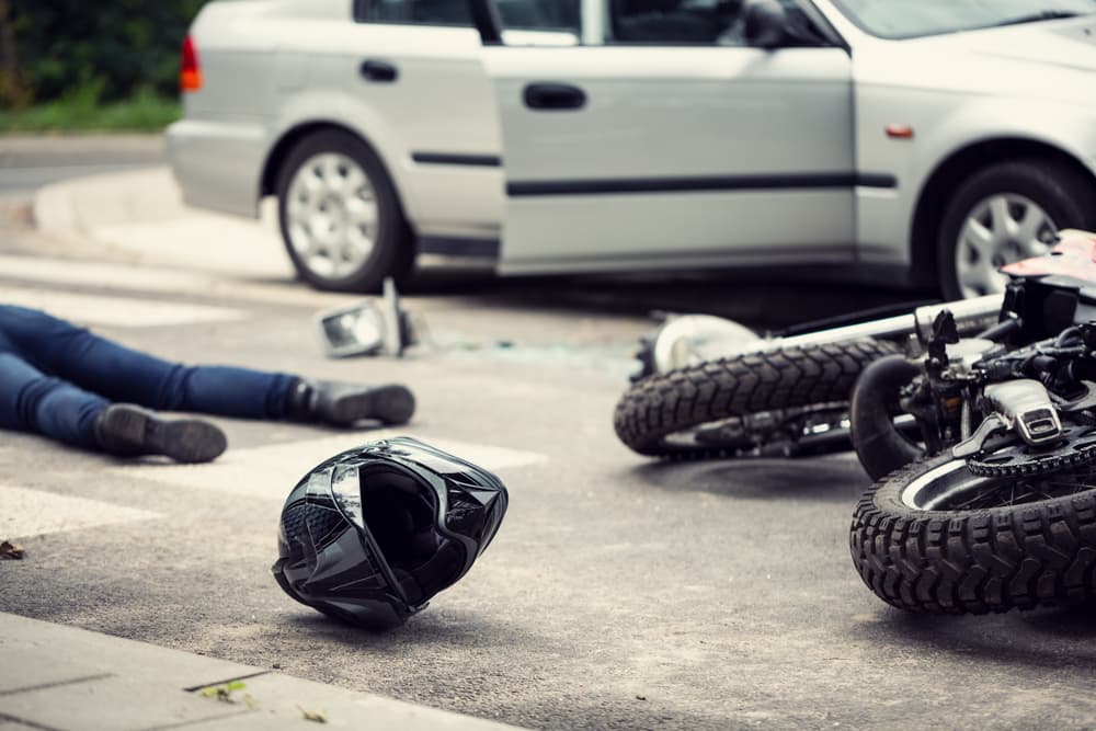 Motorcycle crash scene with helmet on ground and injured person in background.