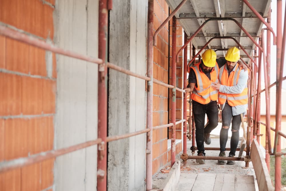 Dos trabajadores de la construcción con equipo de seguridad ayudándose mutuamente en un andamio en una obra.