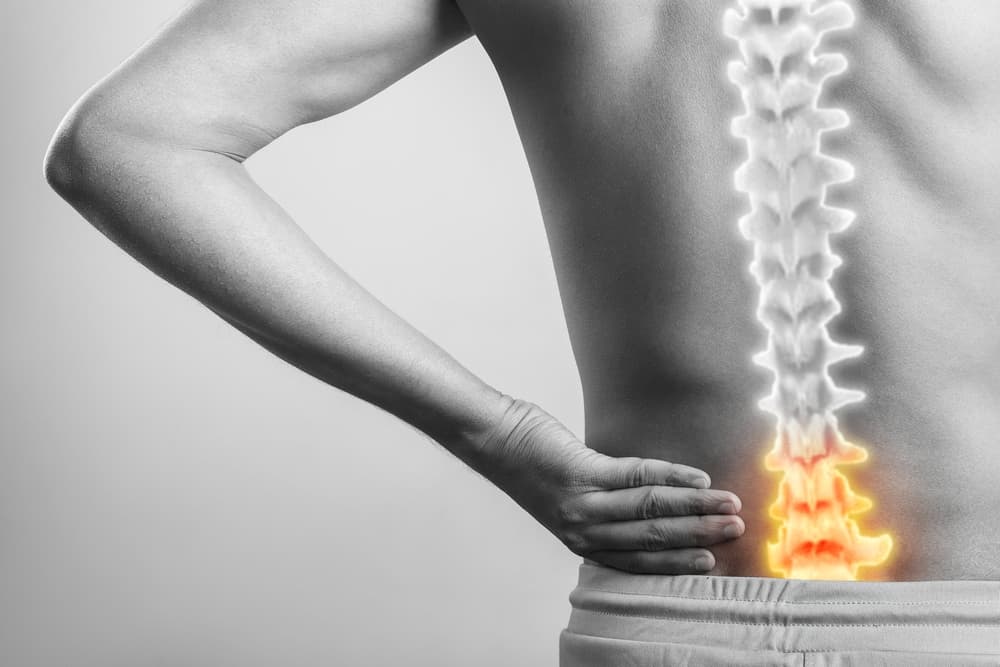 Person holding their lower back with an illustrated spine showing highlighted area of pain.